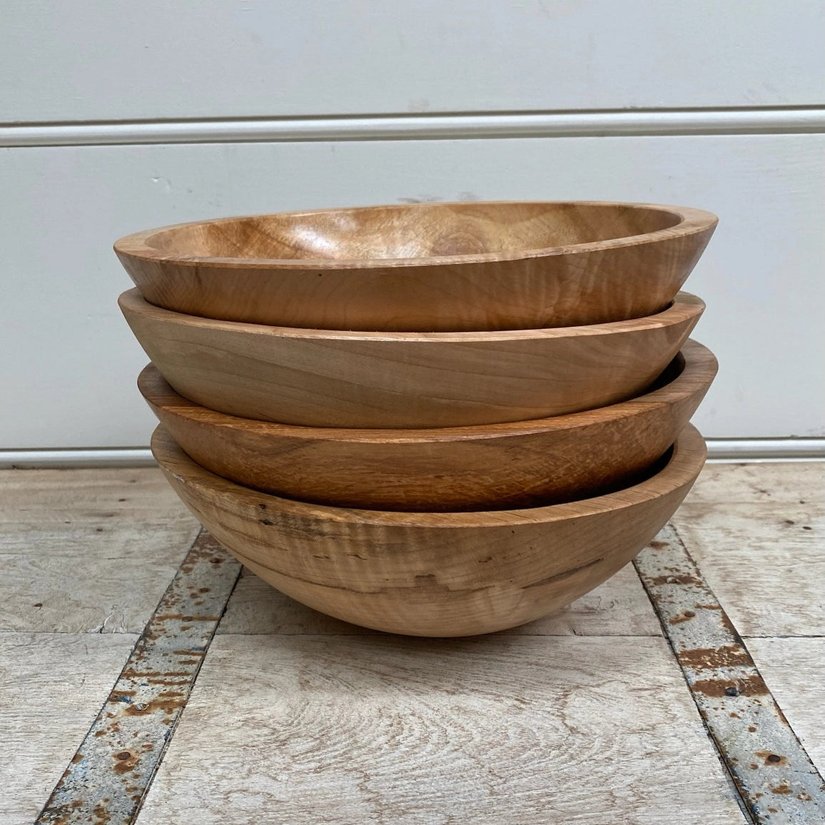 Stack of wooden bowls on a wooden floor with a white wall background