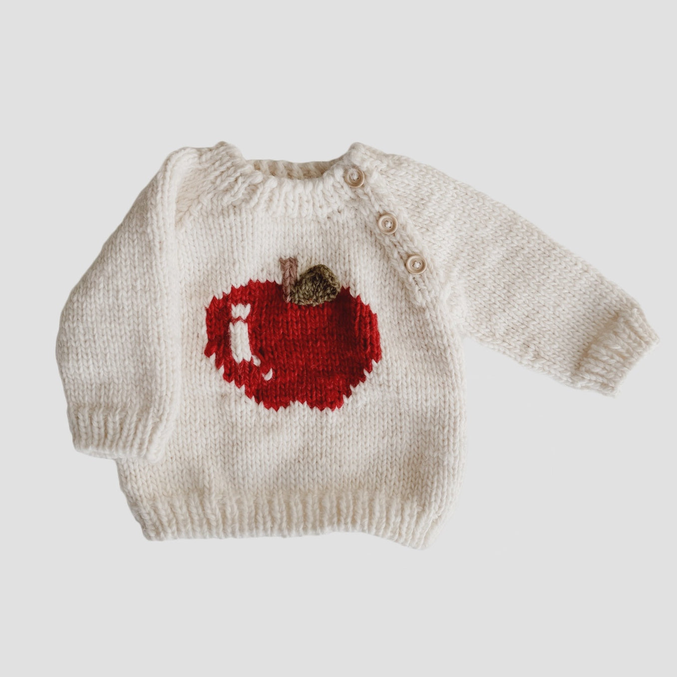 Knitted sweater with a red apple design on a light gray background