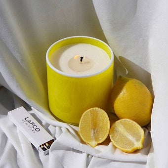 LAFCO White Grapefruit Cabana Candle in bright yellow vessel with fresh lemons on soft fabric.