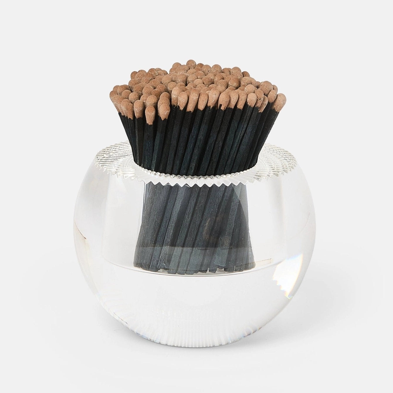 A clear glass bowl-shaped holder filled with black matchsticks topped with tan wooden tips, photographed on a clean white background.