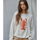 Woman wearing a sweater with a lobster design against a plain background