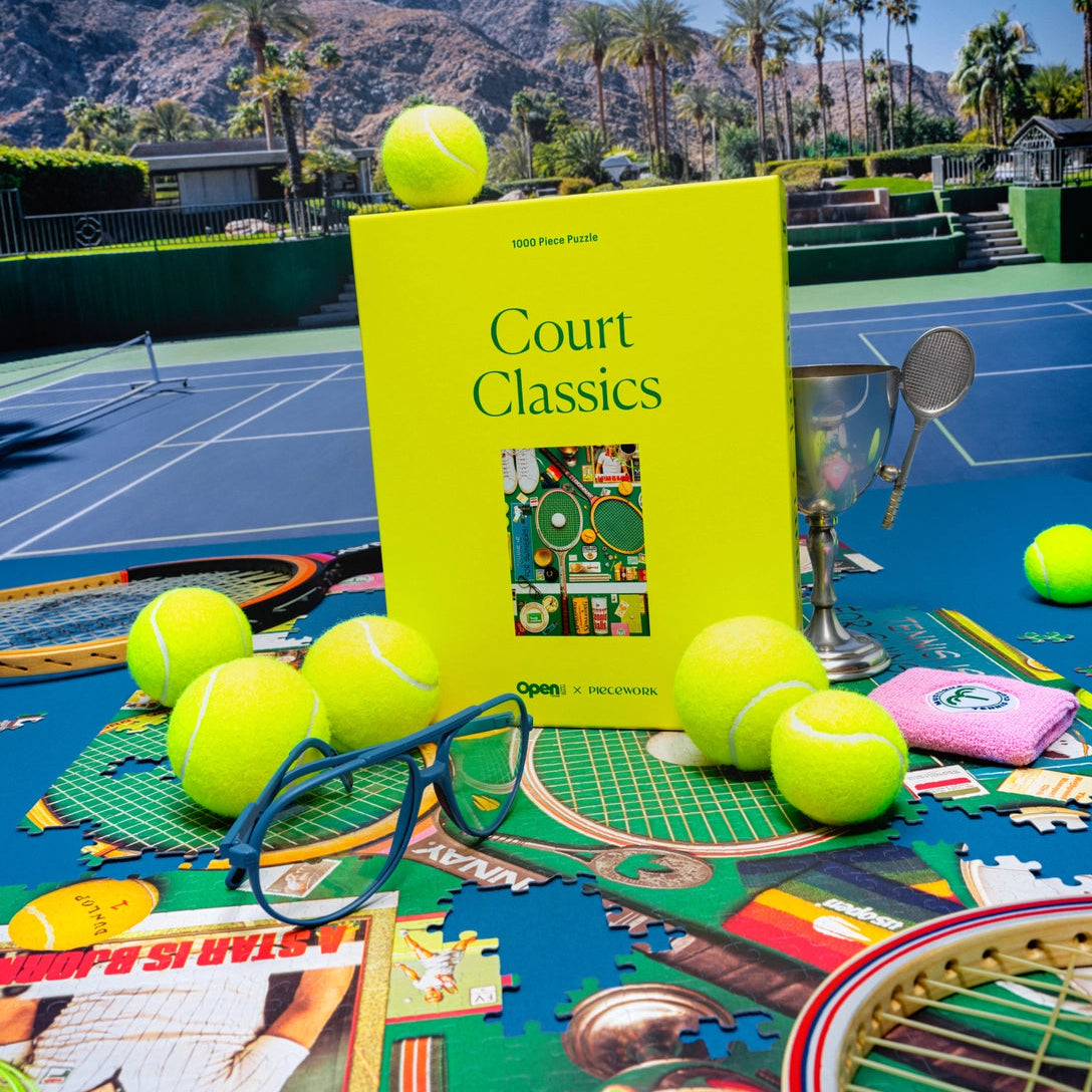 Book titled 'Court Classics' on a tennis court with tennis balls and a racket.